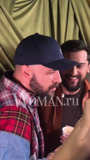 Несколько мужчин беседуют в коридоре презентации; один в бейсболке, другой улыбается на фоне брендового декора мероприятия.