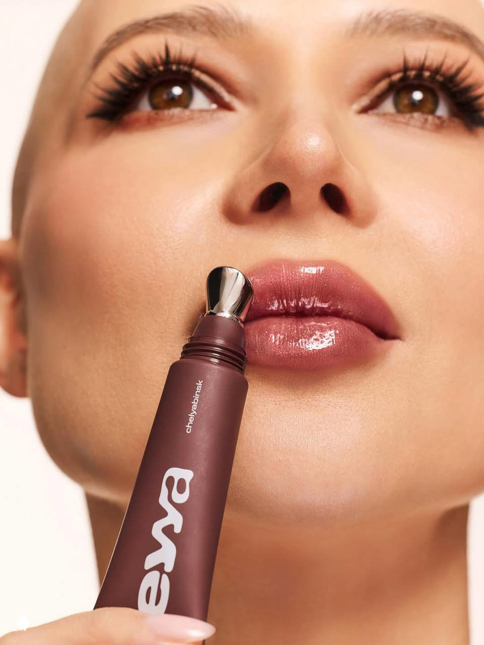 Ещё рекламное фото: крупный план губ и аппликатора тюбика с логотипом бренда, демонстрирующее блеск и внешний вид косметического средства.
