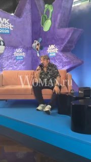 Человек в повседневной одежде сидит на диване на сцене мероприятия VK Fest; на заднем плане видны сценическое оформление и логотипы.