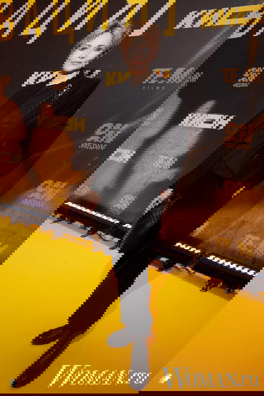 Гостья в чёрном костюме и ботинках позирует у брендволла премьеры «Резервация»; сдержанный и лаконичный вечерний лук.