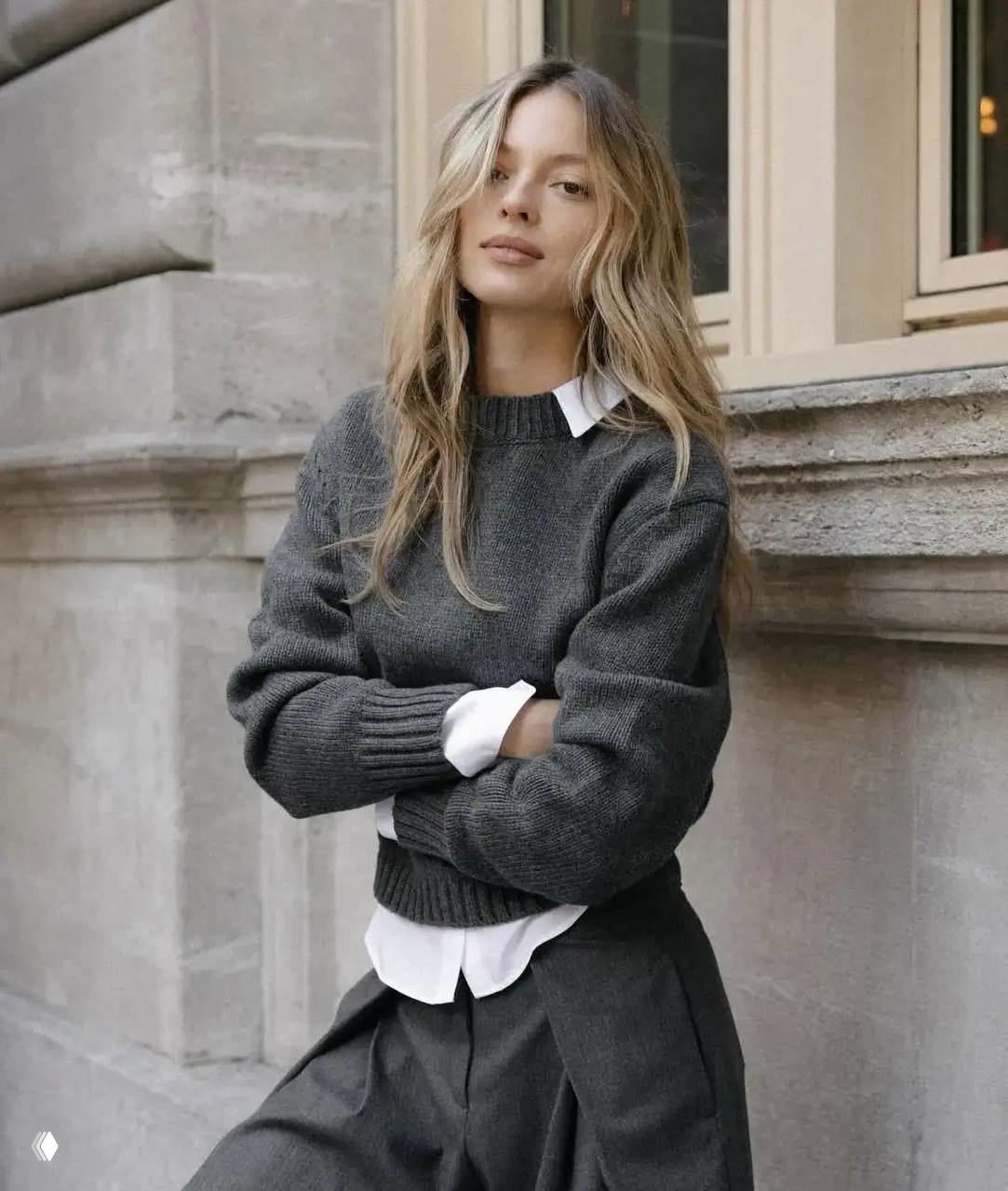 Портрет швейцарской модели Луизы Лаеммель в сером свитере и белой рубашке у каменной стены, натуральный макияж.