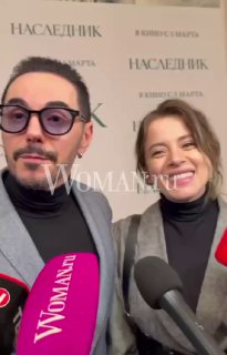 Два человека на пресс‑показе улыбаются у брендированного баннера; на переднем плане несколько микрофонов с логотипом Woman.ru и плакат мероприятия.