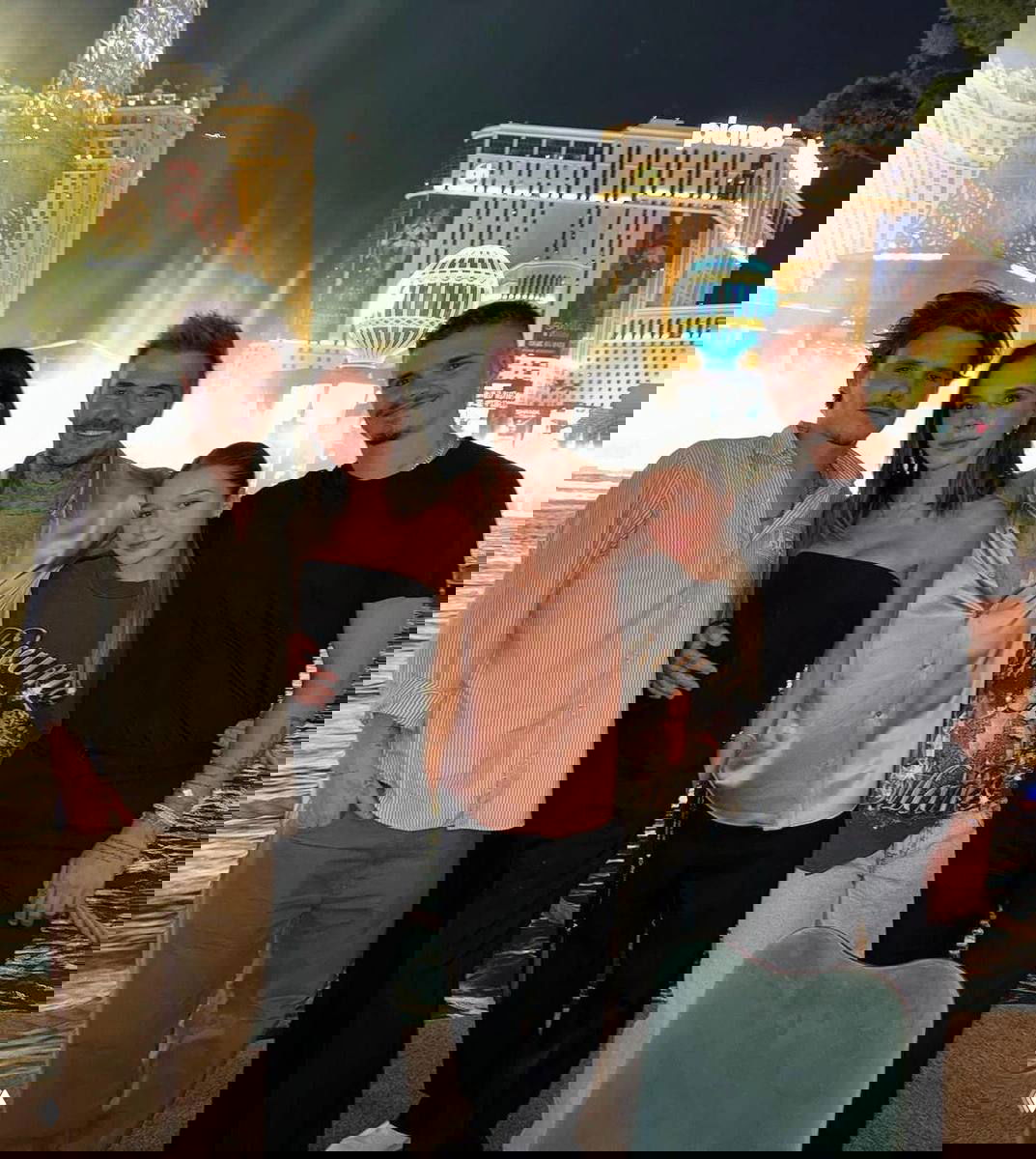 Ночная уличная фотография: несколько человек позируют на фоне подсвеченного фонтана и фасадов отелей, непринуждённые позы и повседневная одежда.