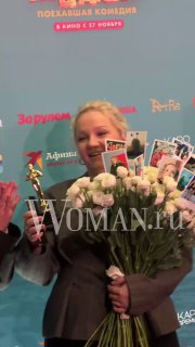 Варвара Щербакова улыбается, держит букет белых цветов и шуточную статуэтку «Оскар» на премьере «По‑братски».