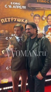 Виктор Логинов и Александр Метелкин улыбаются на красной дорожке премьеры «Петрушка», на заднем плане виден баннер с датой релиза.