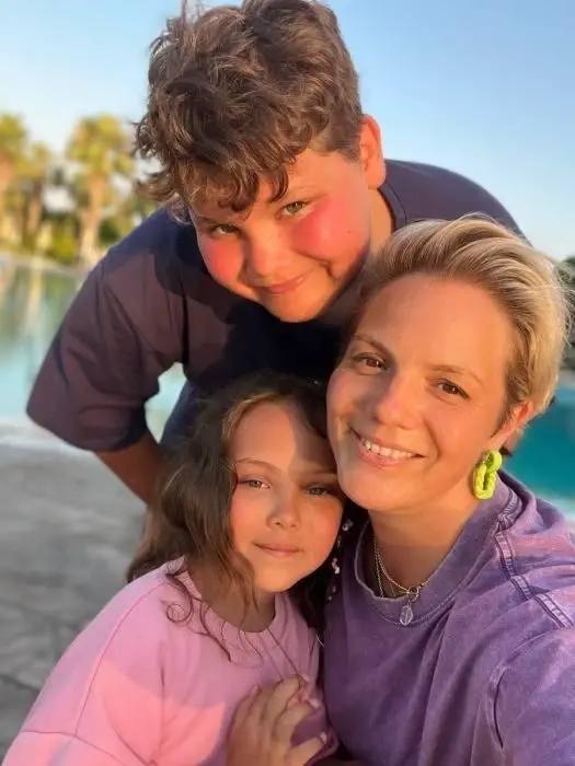 Групповая фотография на открытом воздухе: взрослая женщина и двое детей у водоёма в тёплом естественном освещении