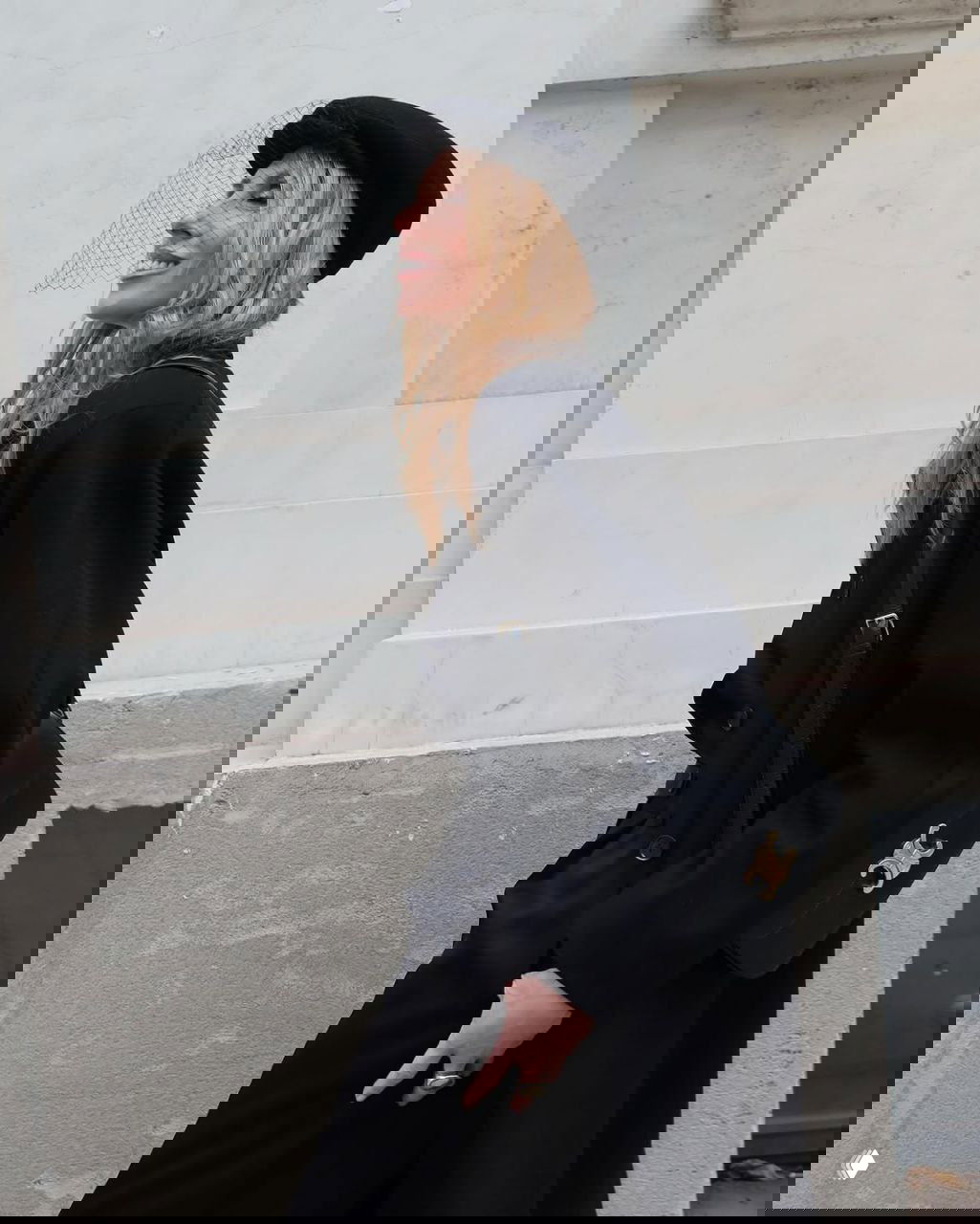 Боковой профиль: Светлана Бондарчук в черном пальто и берете с сеткой, шагает по тротуару, динамичный кадр у фасада здания.