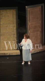 Сцена спектакля «Покровские ворота»: одна актриса в светлом костюме у декоративных дверей, образ Маргариты Павловны, виден логотип Woman.ru.