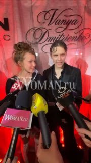 Анна Пересильд и Ваня Дмитриенко на красной пресс‑зоне, перед ними репортеры с микрофонами и логотипами, заметен водяной знак WOMAN.ru.
