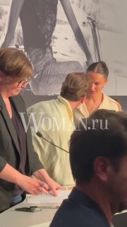 Кадр с близкого ракурса: Майкл Фассбендер и Алисия Викандер общаются за столом на мероприятии в рамках Каннского кинофестиваля, логотип Woman.ru виден.