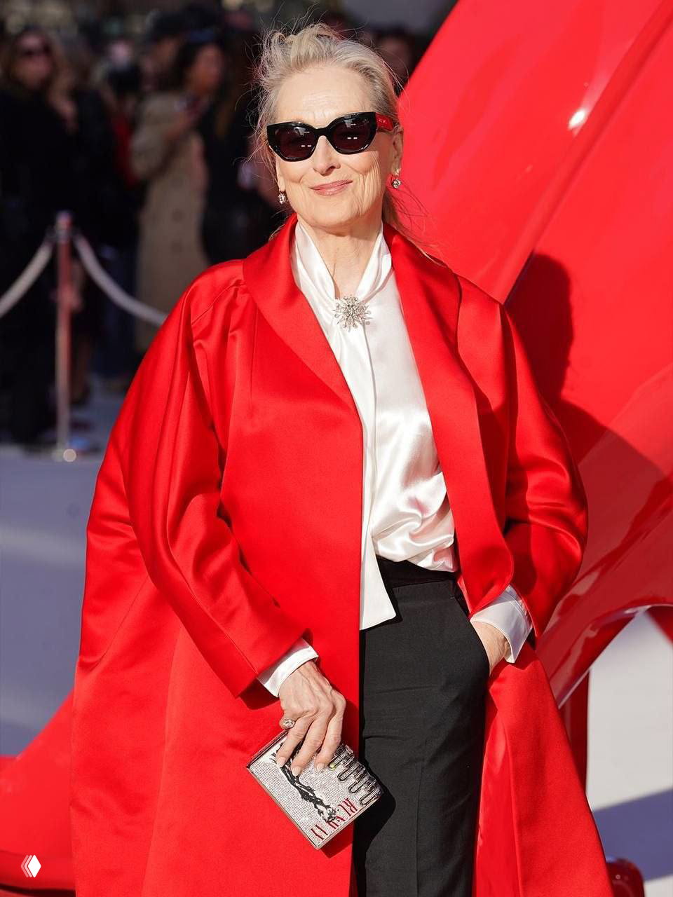 Мерил Стрип в красном плаще и тёмных очках позирует на красной дорожке премьеры «Дьявол носит Prada 2» в Лондоне с клатчем в руке.