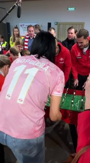 Елена Борщёва в розовой форме играет в настольный футбол на АЗС в рамках экоакции «Чисто. Весна», рядом футболисты и зрители.