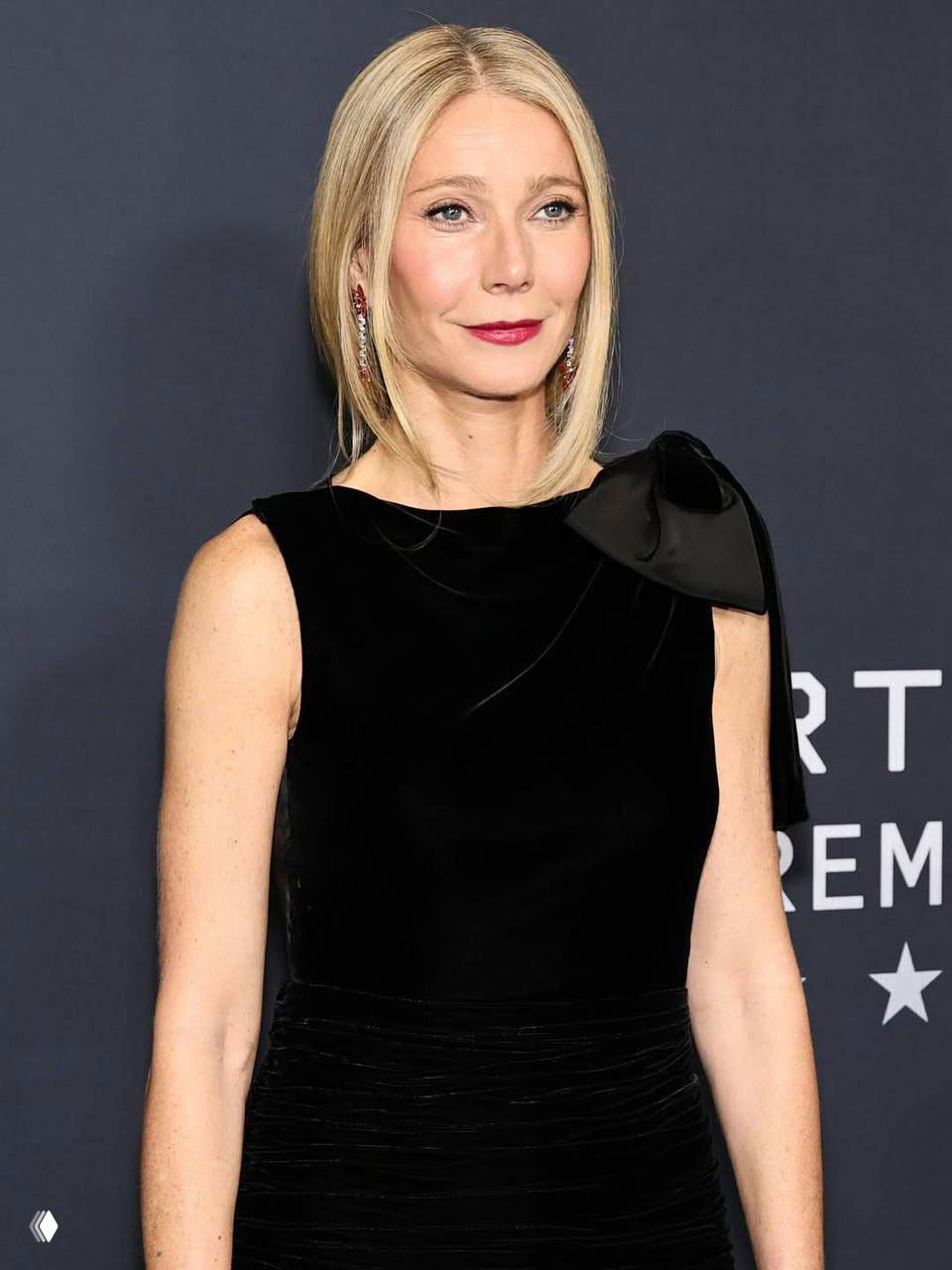 Крупный план Гвинет Пэлтроу в чёрном платье с бантом на плече на красной дорожке премьеры «Марти Суприм» в Нью-Йорке.