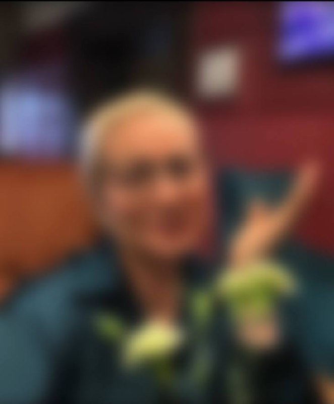 Размытое фото женщины в тёмной одежде с белыми цветами в руках на переднем плане; фон с мягким боке, черты лица неразборчивы.