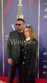 Алексей Чумаков и Юлия Ковальчук на красной дорожке премии BraVo: пара в тёмных образах позирует на фотозоне рядом с тропеем наград.