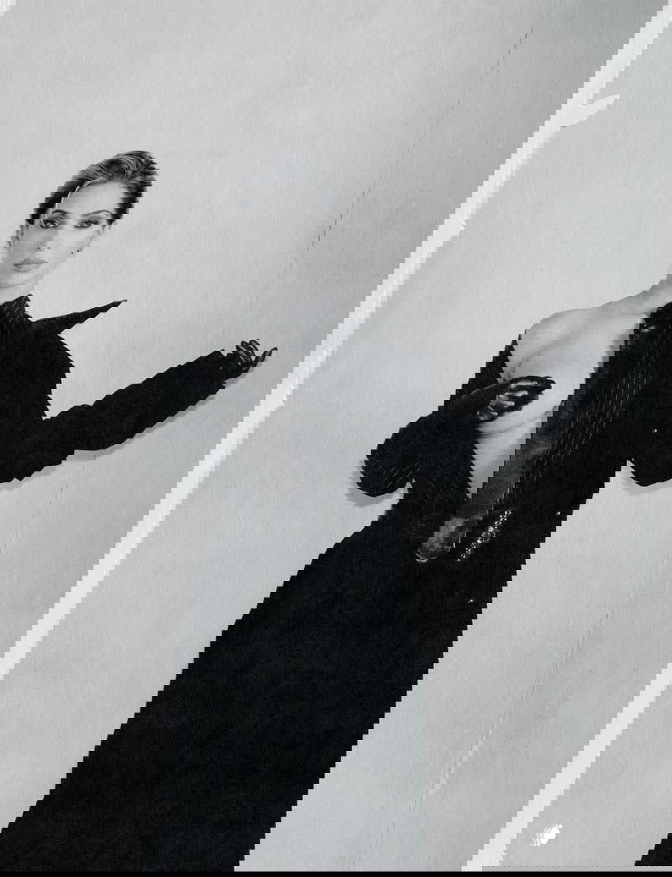 Черно‑белый кадр в полный рост: женщина в тренч‑пальто с открытой грудью и перчаткой — концептуальная мода для глянца.