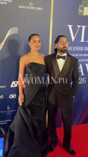 Мот и Мария Мельникова на красной дорожке премии BraVo: музыкант и его спутница в вечерних нарядах позируют на фоне сценического баннера.