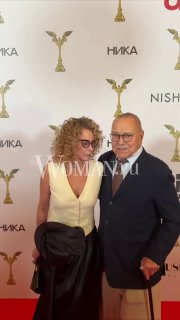 Двое гостей в элегантных костюмах позируют у брендволла на церемонии «Ника», снимок сделан с красной дорожки в портретной композиции