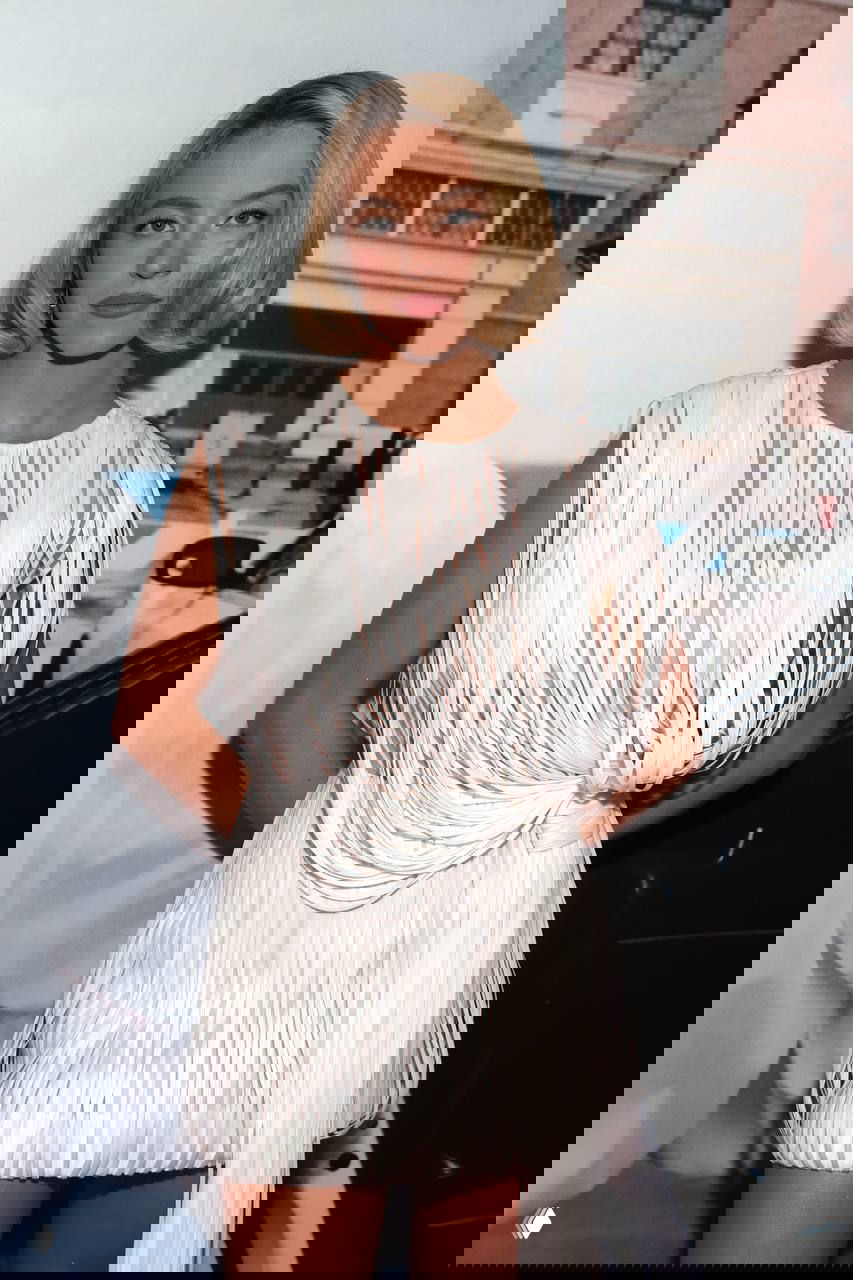 Сидни Суини в белом платье с бахромой и короткой стрижкой на официальном пре‑пати «Золотого глобуса», на фоне городского фасада и фотозоны.