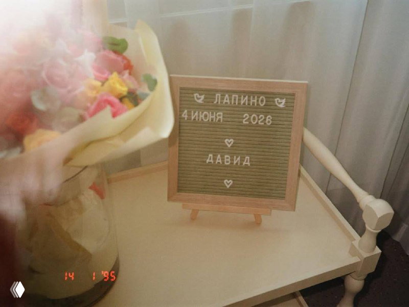 Декор и табличка с надписью «Лапино 4 июня 2026 Давид» рядом с букетом цветов на тумбочке — имя и дата рождения новорождённого
