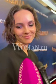 Крупный план Стаси Милославской во время интервью на премьере фильма «Красавица», в кадре микрофон и фон с постером.