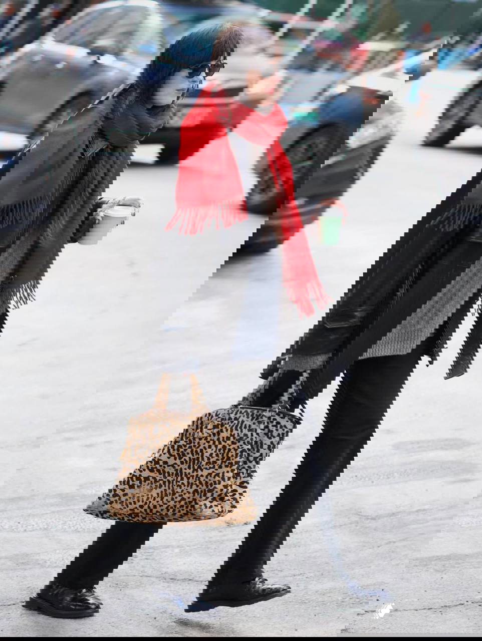 Дакота Джонсон шагает по улице в том же образе: солнцезащитные очки, красный шарф, леопардовая сумка и бумажный стакан кофе в руке.