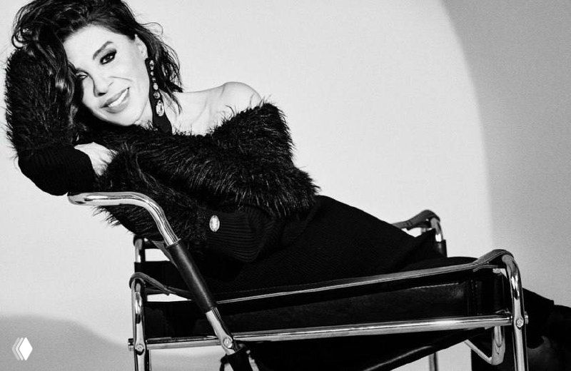 Чёрно‑белый кадр Небахат Чехре в сидячей позе, фешн‑стилизация с меховым элементом и глитч‑искажением в композиции.