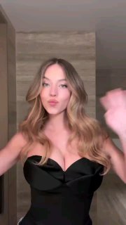 Кадр видеоролика: девушка в чёрном платье с волнистыми волосами и мягким естественным макияжем на нейтральном фоне, демонстрация образа.