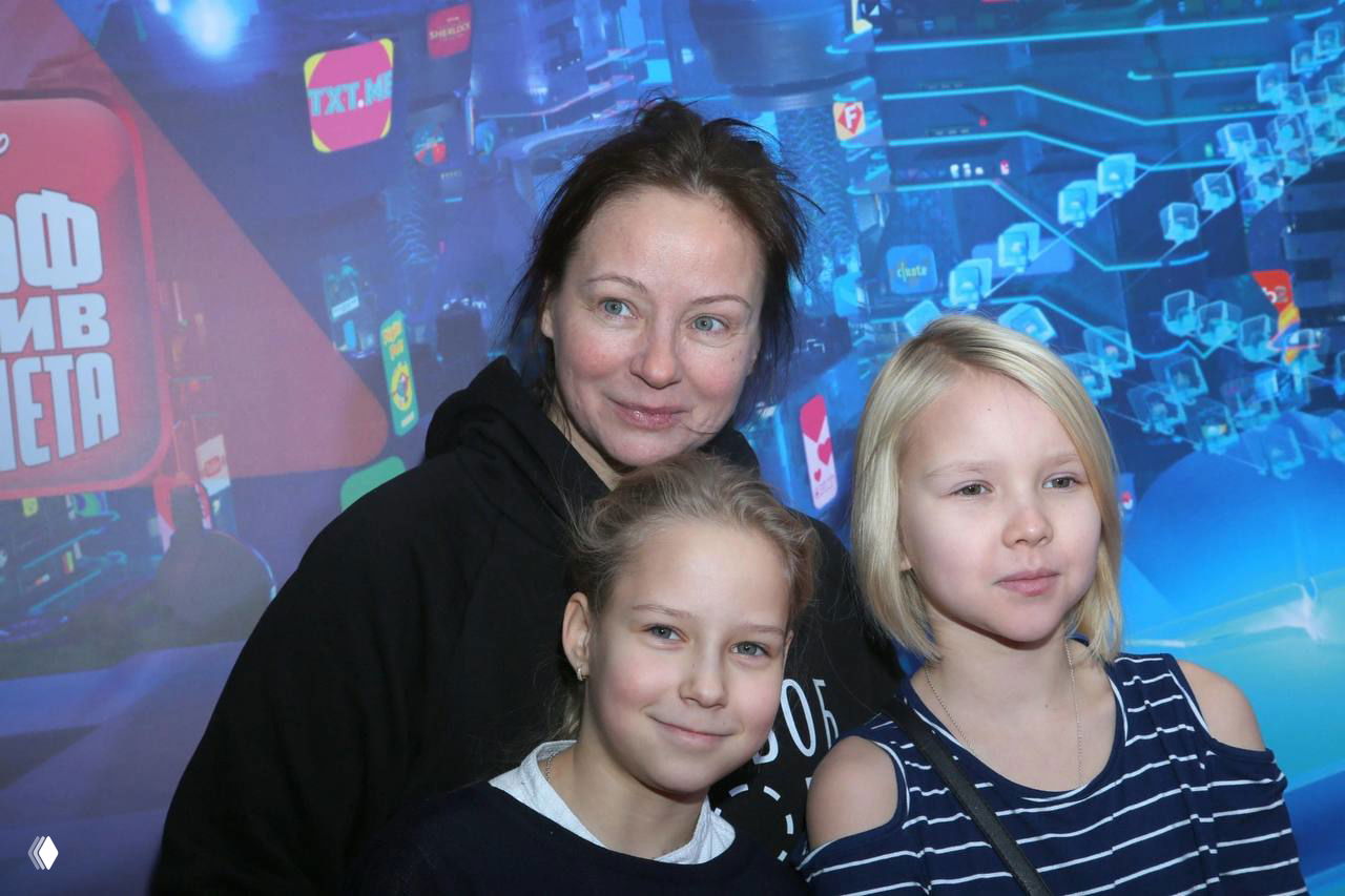 Евгения Добровольская с двумя девочками на светлом фоне семейного или общественного события: тёплая атмосфера, повседневная одежда, дружеские улыбки.