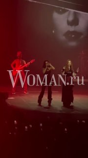 Снимок с концерта «Тату» в Москве: два участника на сцене, гитара и большой экран с чёрно‑белым портретом, публика и логотип Woman.ru в кадре