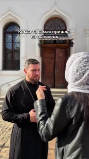 Мужчина в церковном облачении у входа в храм беседует с женщиной; у стены видны архитектурные арки дверей православного храма.