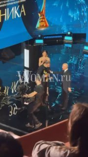 Момент церемонии на сцене: ведущие и лауреат при вручении премии «Ника», сцена и зрители, водяной знак WOMAN.ru