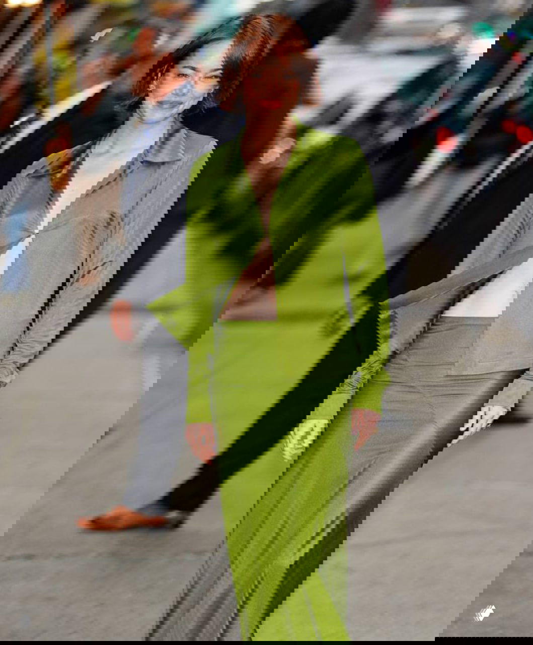 Актриса в зелёном костюме идёт по городскому тротуару — уличный снимок в полный рост с естественной позой и лёгкой улыбкой.