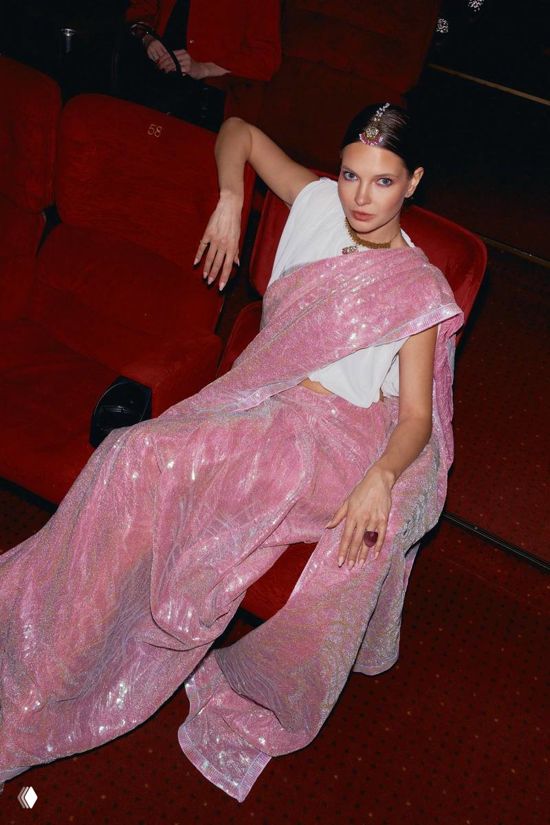 Женщина в розовом блестящем сари расположилась в красных креслах кинотеатра на премьере музыкальной комедии, кадр из зрительного зала.