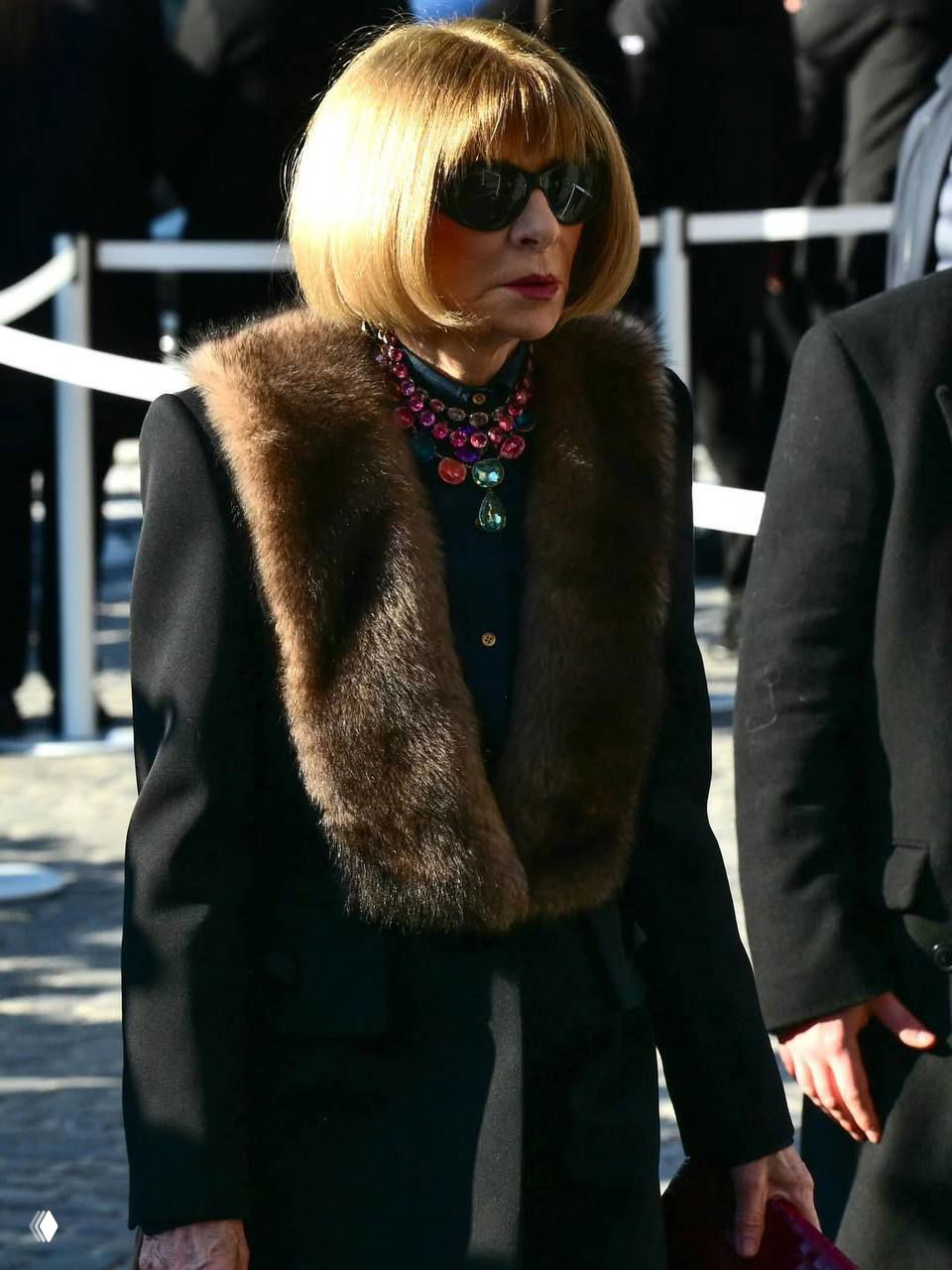 Леди в элегантном тёмном пальто с меховой накидкой и декоративным ожерельем на фоне улицы Рима во время прощания.