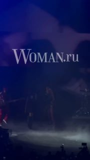 Фото с концерта «Тату»: сцена в дымке, группа на фоне синего освещения и силуэты музыкантов, логотип Woman.ru виден поверх изображения