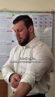 Мужчина в светлой рубашке закатывает рукав на фоне доски с заметками; кадр напоминает бытовое вертикальное видео из аккаунта в соцсетях.