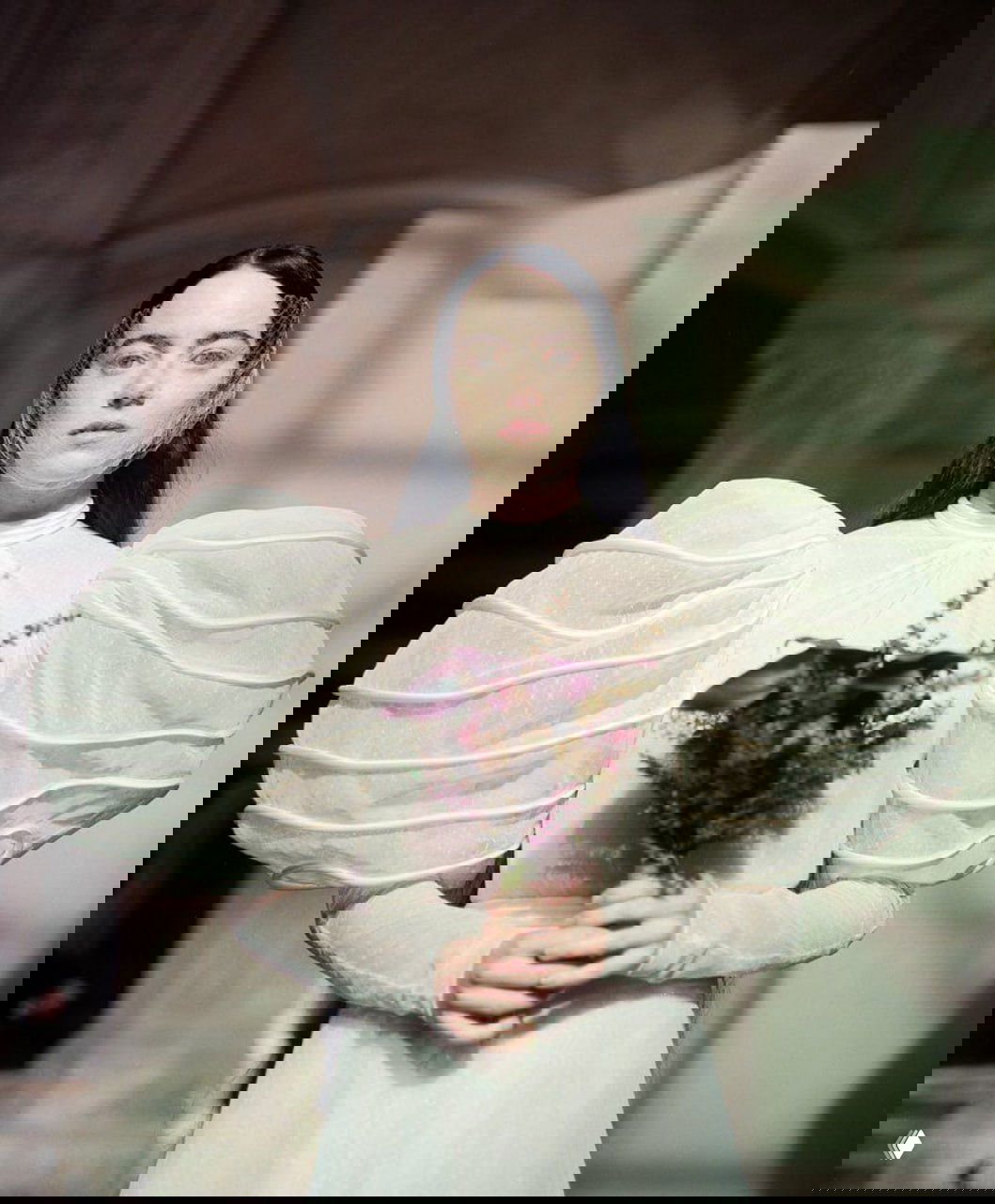 Портрет в свадебном или готическом стиле: актриса в светлом платье с объёмными рукавами держит букет, задумчивый образ на фоне интерьера.