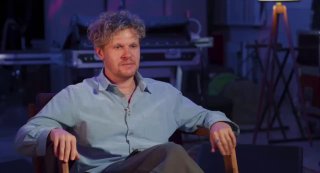 Ваня Дмитриенко сидит в кресле в студии во время интервью: расслабленная поза, сценическое освещение и видимое съемочное оборудование вокруг.