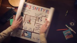 Руки держат лист с нарисованным сторибордом и схемой на рабочем столе; видны маркеры, скотч и блокнот.