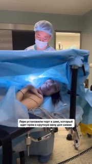 Операционная: женщина на столе под стерильным покрывалом, медперсонал в масках устанавливает порт для химиотерапии.