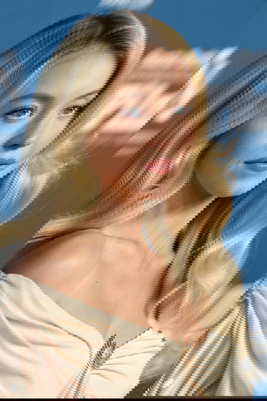 Крупный план лица Сидни Суини на фестивале: гладкая кожа, нюдовый макияж, ретро‑локоны и брошь на декольте кремового платья в стиле 50-х.