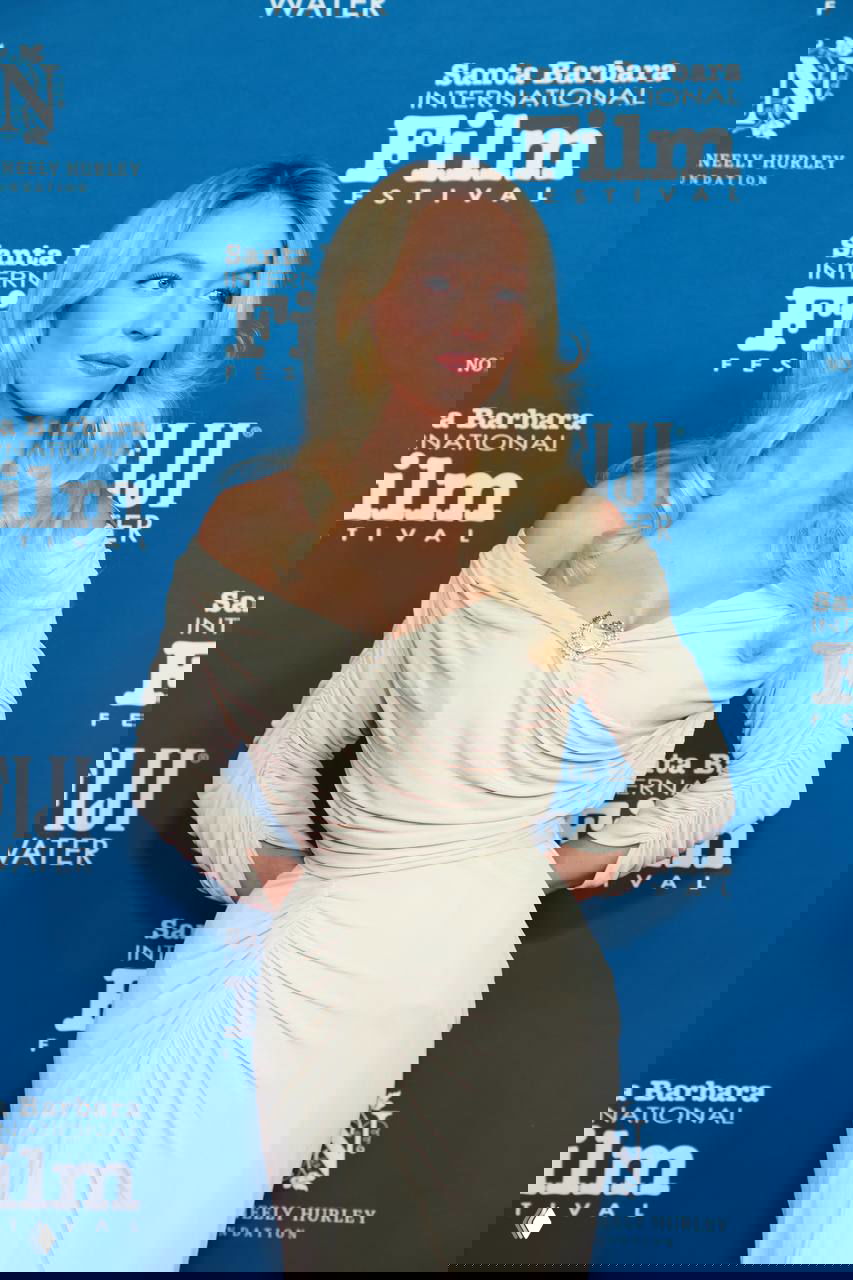 Сидни Суини в три четверти на фоне баннера Santa Barbara International Film Festival: драпировка платья, подчеркнутая талия и светлые волнистые волосы в ретро‑стилистике.