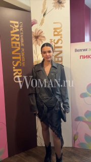 Участница public-talk «Дети будущего» стоит у бренд-стенда Parents и Woman.ru в фойе мероприятия, вечерняя одежда и фотозона