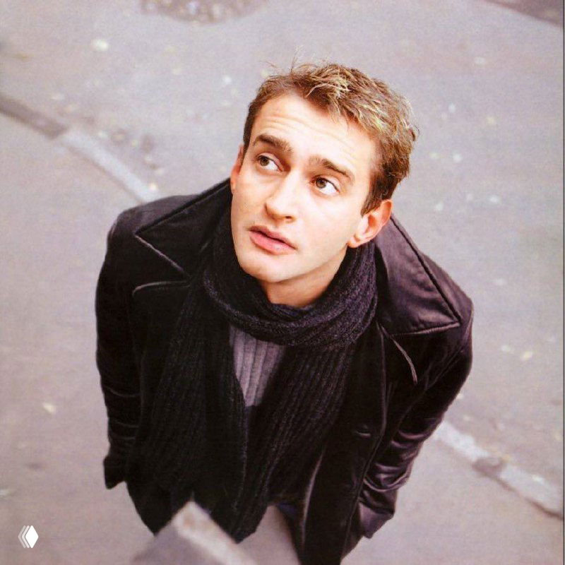 Студийный портрет мужчины в тёмной куртке и шарфе, кадр сделан сверху, фон городской тротуар, естественный городской контекст съёмки.