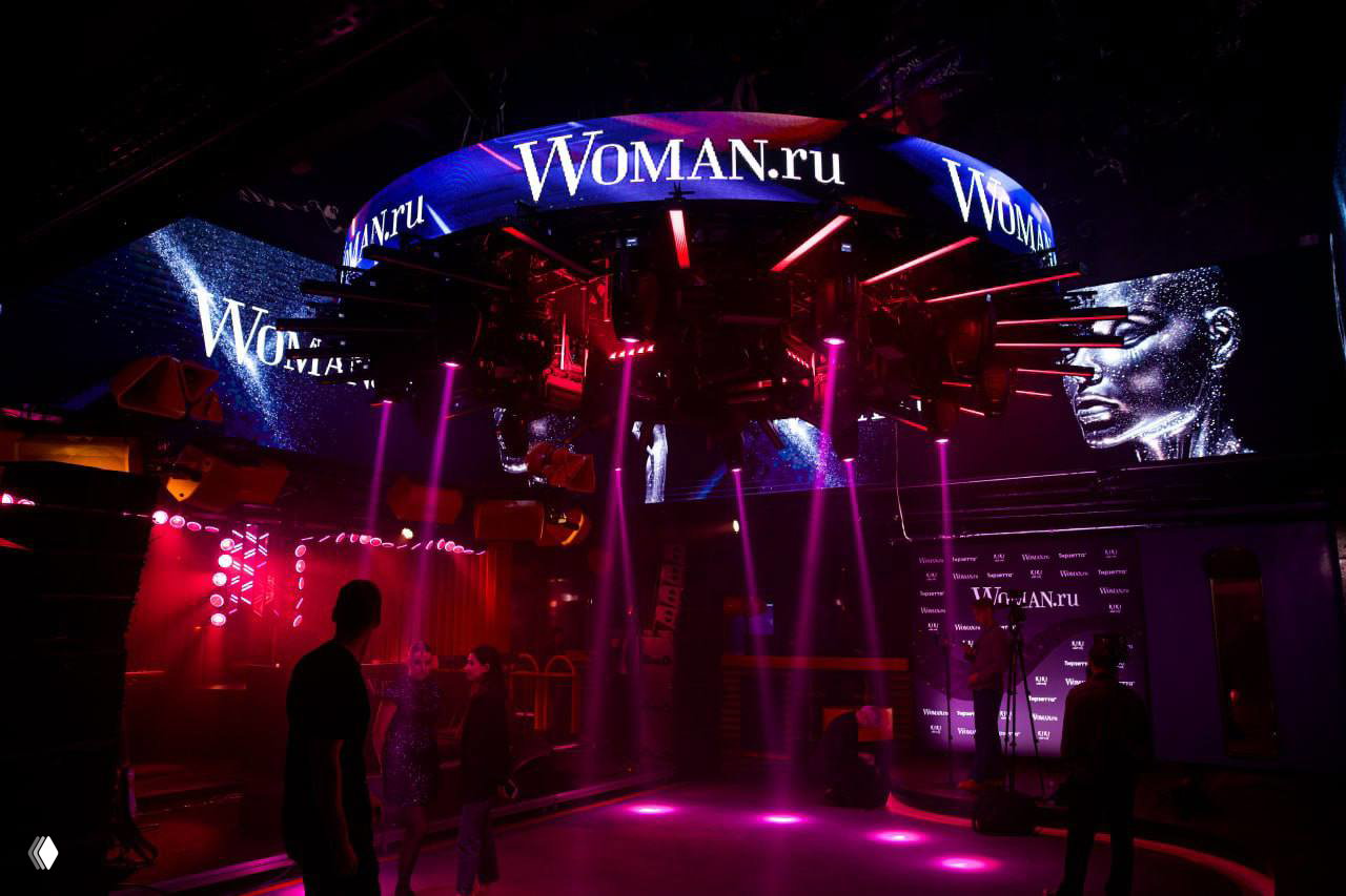 Интерьер KiKi Event Dom с большой круглой LED-панелью и логотипом Woman.ru; пустой танцпол в пурпурно-фиолетовой подсветке и подготовка к вечернему событию.
