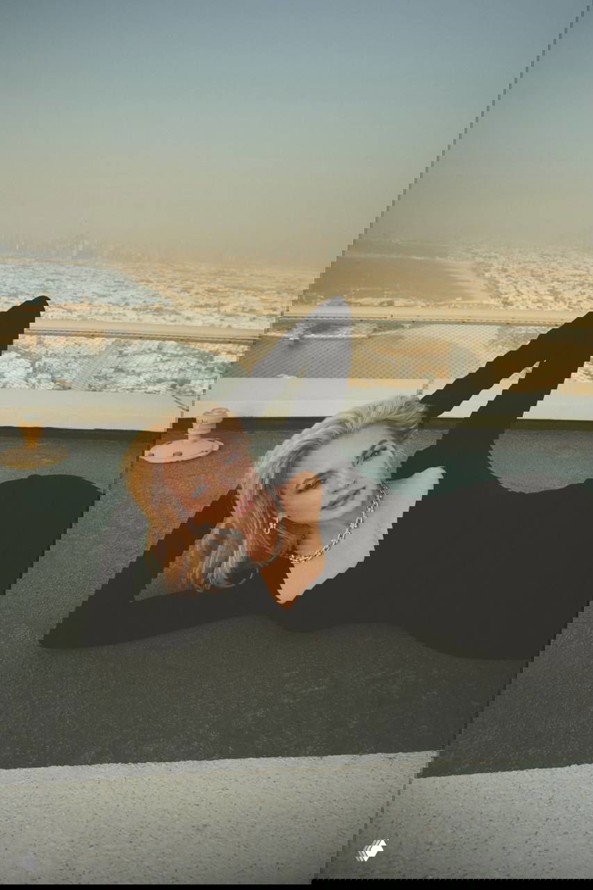 Линдси Лохан в облегающем чёрном платье лежит на фоне городского пейзажа с видом на побережье — элегантный образ для журнала.