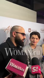 Двое людей у фотостены на публичном мероприятии дают интервью; на переднем плане несколько микрофонов с логотипами, заметна водяная маркировка.