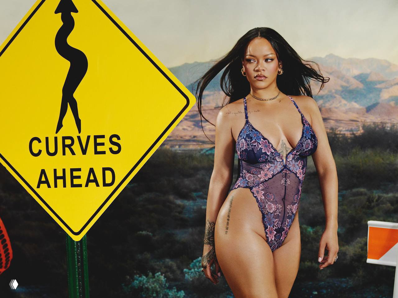 Рианна в прозрачном кружевном боди стоит рядом со знаком «Curves Ahead», поза в полный рост на фоне пустынного задника кампании.
