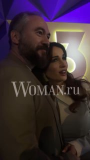 Крупный план Анфисы Чеховой и Александра Златопольского на презентации «ТВ-3»: пара улыбается в камеру, на снимке виден водяной знак Woman.ru и фиолетовая подсветка.